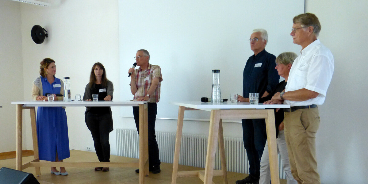 Teilnehmerinnen und Teilnehmer der Podiumsdiskussion stehen an Stehtischen auf dem Podium