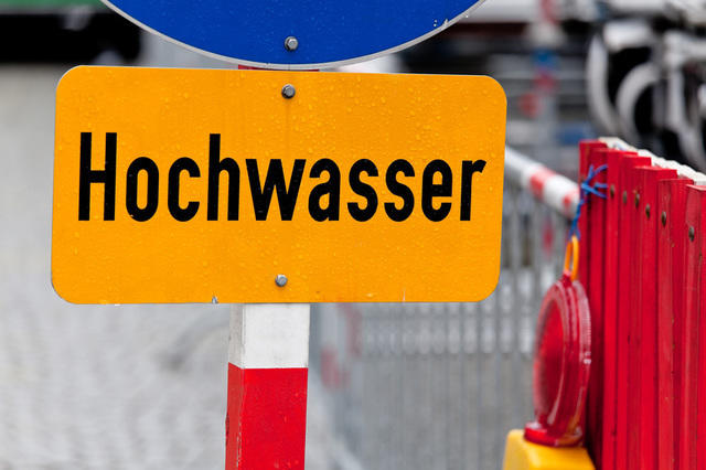 Ein gelbes Schild auf dem mit schwarzer Schrift das Wort Hochwasser zu lesen ist.